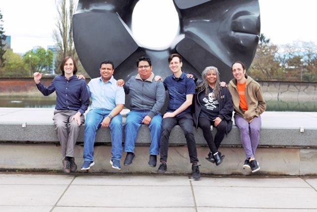 The Agaric team sitting in front of Seattle's iconic "black hole" statue with our hands on each other's shoulders. Ben, in character, placing his hand on a non-existent person's shoulder next to him.