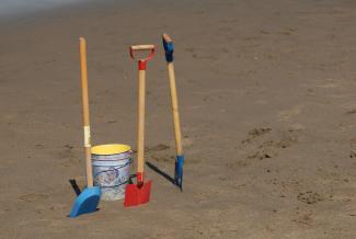Three beach shovels standing up in the sand next to a pail.