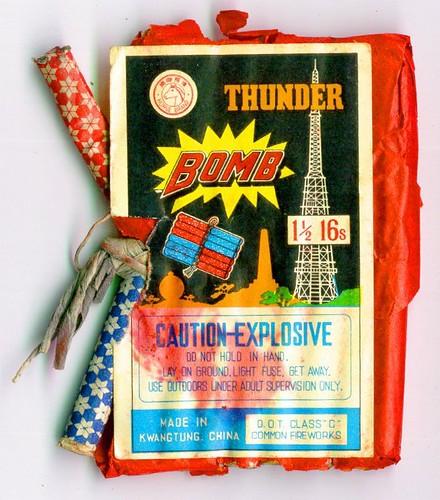 Old-fashioned half-used colorful red and blue fireworks box, labeled 'Thunder Bomb' with the warning Caution-Explosive in large capitalized letters.